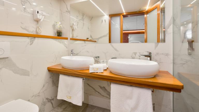 Ein helles Badezimmer mit weissem Marmor, ovale Waschbecken und grossem Spiegel an der Wand.